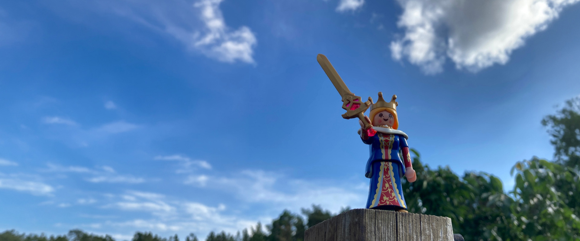 Kleine Spielfigur als Königin mit Schwert vor blauem Himmel und Wolken.