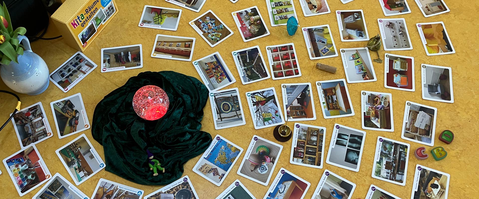 Viele Bildkarten mit Raumgestaltungsbeispielen und ein leuchtender roter Ball auf grünem Samttuch bei einer Fortbildung von Susanne Jimenez.