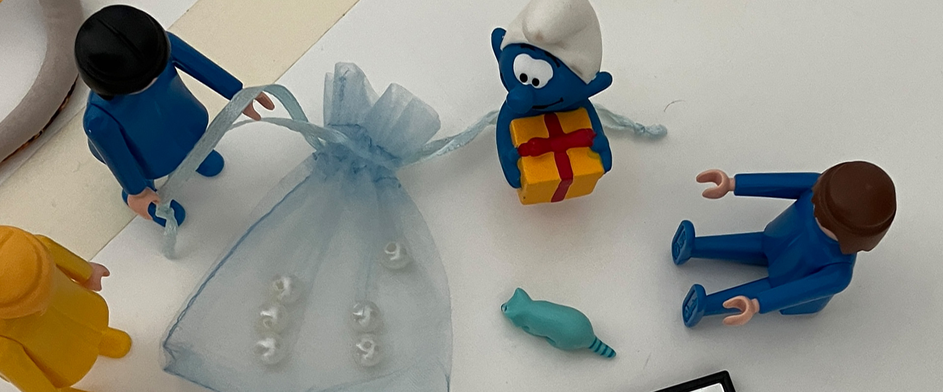 Spielfiguren und Symbolobjekte wie ein kleines Geschenk, Schlumpf und Holzperlen als Metapher für Vorurteilsfreiheit und Vielfalt.