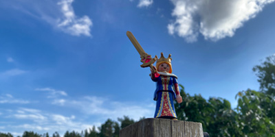 Kleine Spielfigur als Königin mit Schwert vor blauem Himmel und Wolken.