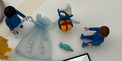 Spielfiguren und Symbolobjekte wie ein kleines Geschenk, Schlumpf und Holzperlen als Metapher für Vorurteilsfreiheit und Vielfalt.